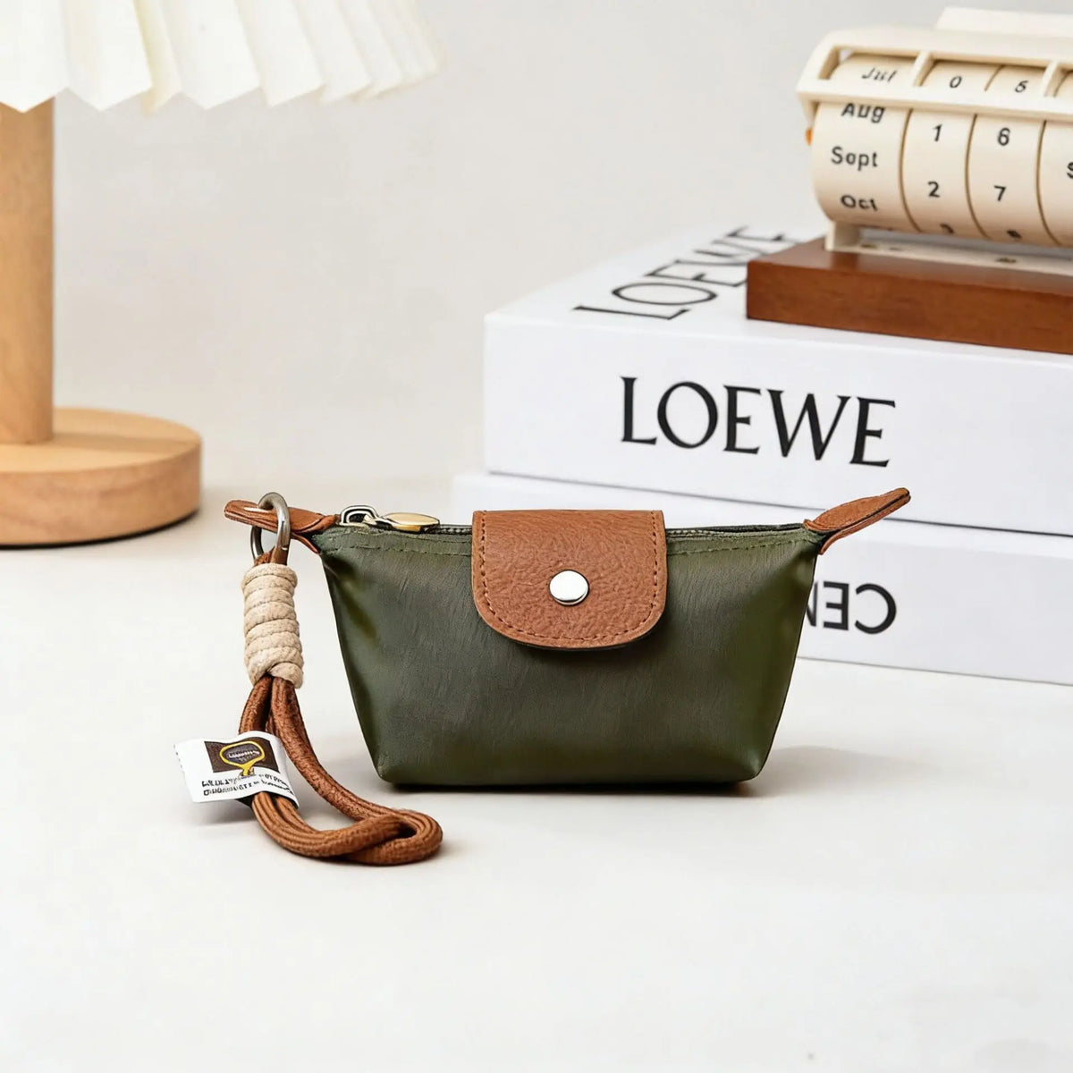A dark olive green compact coin purse with a brown leather flap and braided cord strap resting on a white surface.