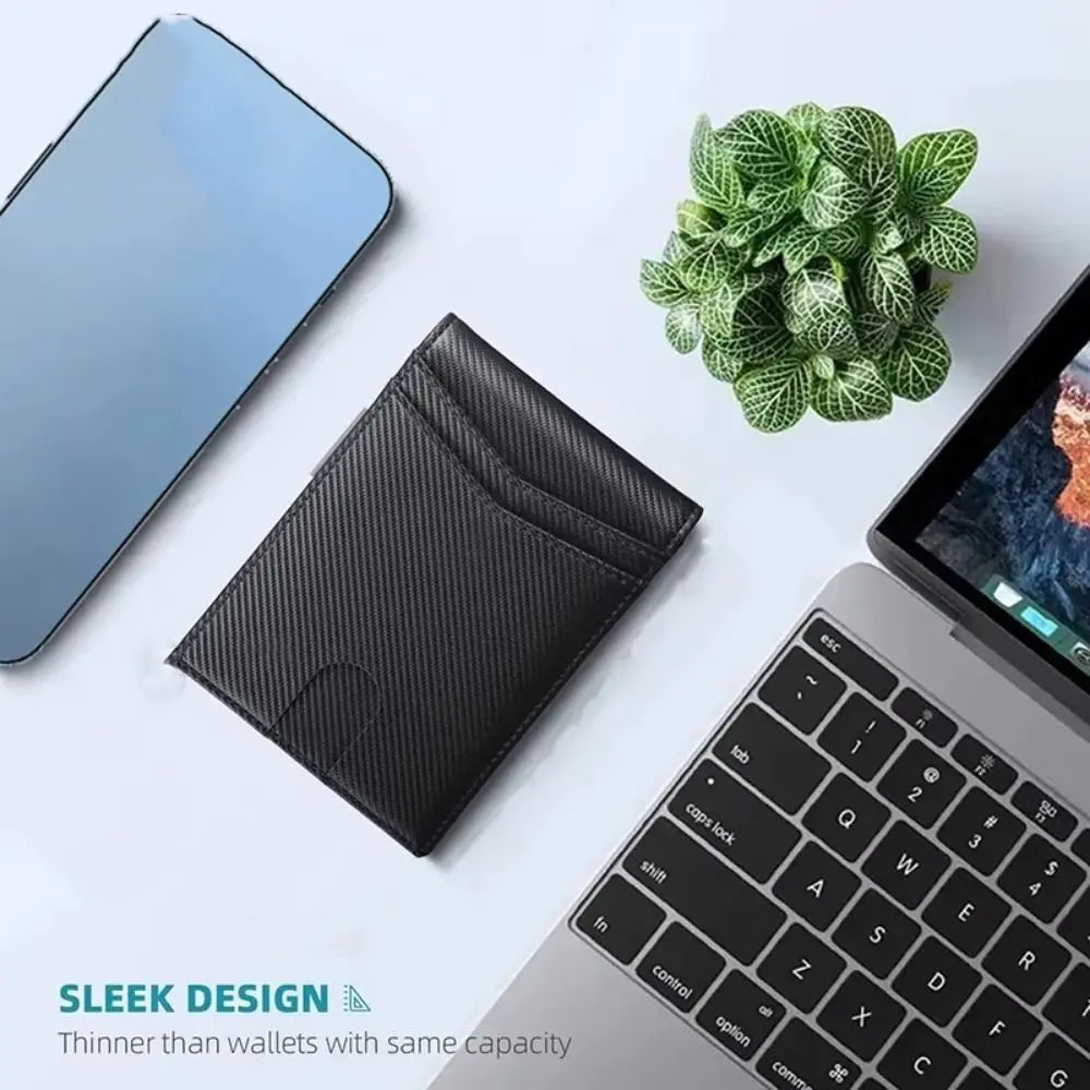 A black slim wallet is shown next to a silver smartphone and a potted green plant on a white surface.