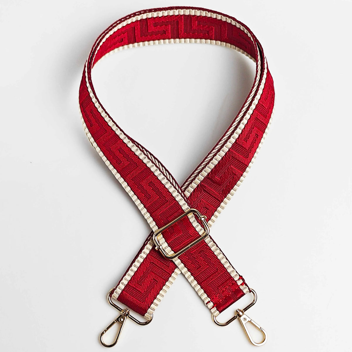 A red and white patterned adjustable crossbody bag strap with a gold buckle and metal hardware.