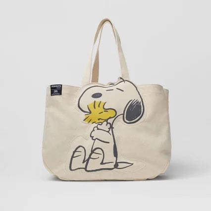 A beige canvas shoulder bag featuring a cartoon drawing of Snoopy.