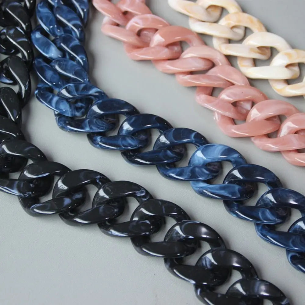 A close-up of multiple acrylic resin detachable bag chain straps in shades of black, dark blue, pink, and cream.