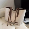 A beige canvas shoulder tote bag with brown leather trim resting on a white quilted surface.