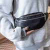A person holds a black nylon crossbody sling bag against a gray sweatshirt.