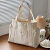 Una bolsa de tela beige con correas color canela sobre una superficie de madera junto a una planta en maceta.