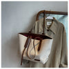 A beige canvas shoulder tote bag is displayed hanging on a wooden hanger against a white wall.
