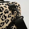 Close-up of a black leather strap and zipper detail on a beige leopard print travel duffel bag.