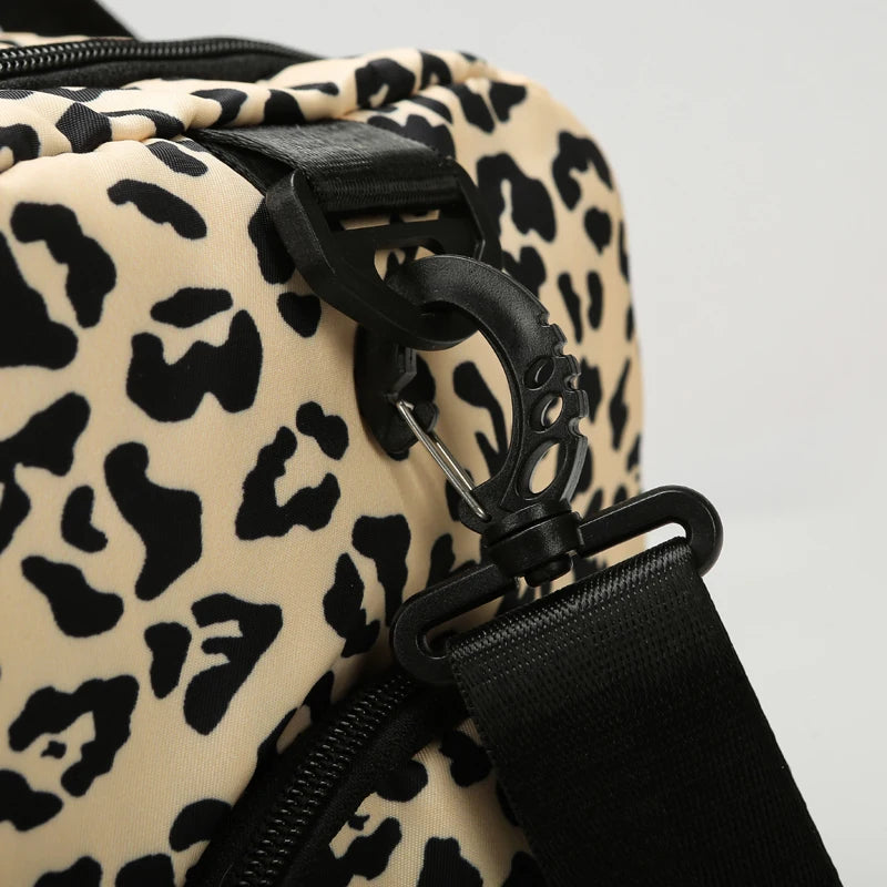 Close-up of a black leather strap and zipper detail on a beige leopard print travel duffel bag.