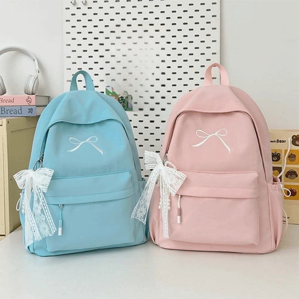 A light blue and pink embroidered backpack with white ribbon details resting on a white surface.