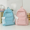 A pink backpack with white embroidery and lace trim is shown next to a light blue backpack on a white surface.