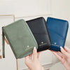 A hand holds a green RFID-blocking passport wallet with a zipper closure and a dark blue one.