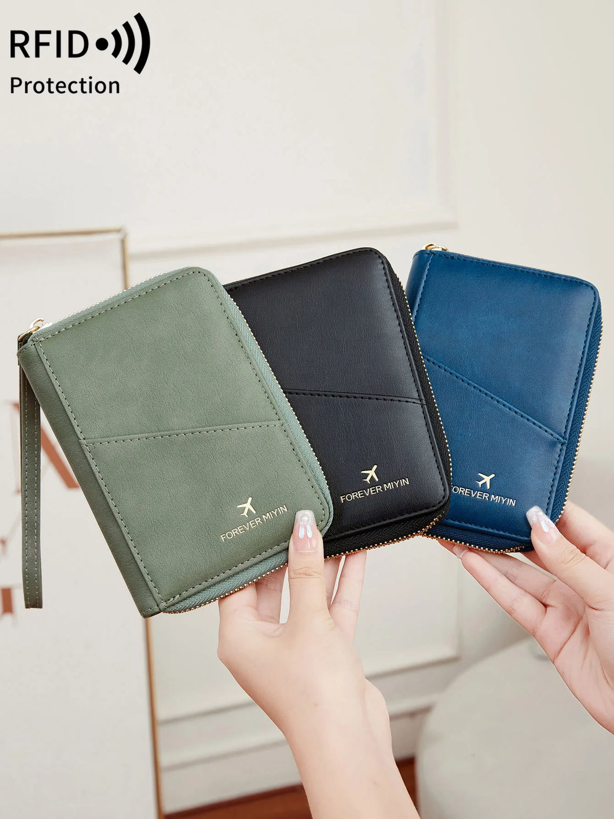 A hand holds a green RFID-blocking passport wallet with a zipper closure and a dark blue one.