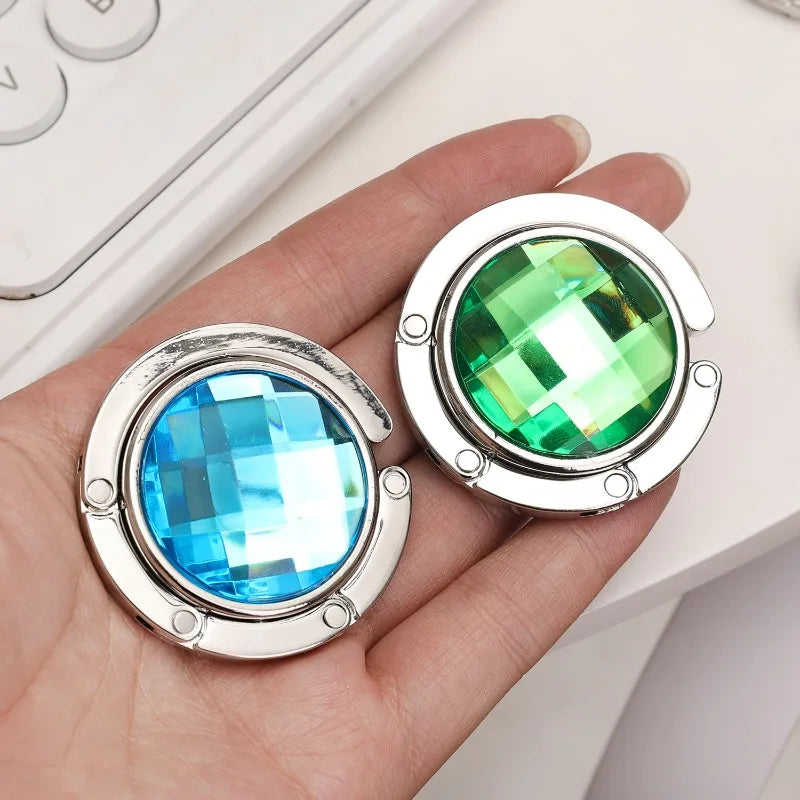A hand holds two round acrylic foldable hooks, one blue and one green, with silver metal findings.
