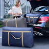 Two navy blue storage bags are placed on the ground next to a black car, with a woman in a white top standing nearby.