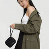 A young woman models a olive green jacket and black skirt while holding a black mini coin purse.