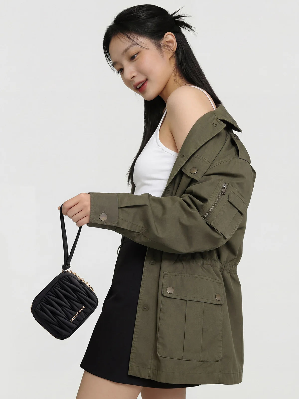 A young woman models a olive green jacket and black skirt while holding a black mini coin purse.