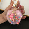 A hand holds a custom initial letter keychain featuring a shiny resin pendant with pink alphabet charms and a fluffy pink pom