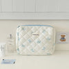 Sac de rangement cosmétique bleu clair en duvet avec motif ours sur le devant, posé sur une surface blanche.