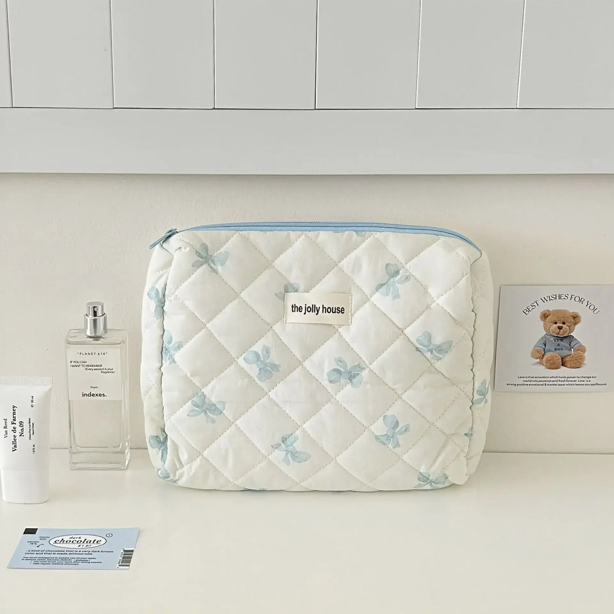 Sac de rangement cosmétique bleu clair en duvet avec motif ours sur le devant, posé sur une surface blanche.