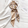 Foulard pour cheveux en soie, motif floral jaune et rose, noué en nœud, posé sur tissu blanc.