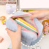 A hand is opening a light blue zippered cosmetic storage pouch filled with pens and pencils.