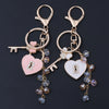 Gold-toned key chain featuring a heart charm and a decorative bow, adorned with clear rhinestones and purple beads.