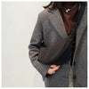 A woman wearing a tweed blazer and brown top holds a black sling crossbody bag.