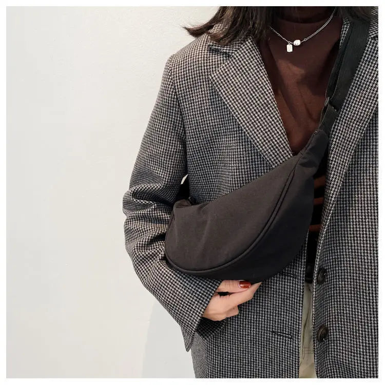 A woman wearing a tweed blazer and brown top holds a black sling crossbody bag.
