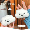 A hand holds a white cloud-shaped plush keychain with brown feet against a wooden background.