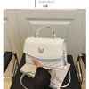 A white women's solid texture shoulder messenger bag is displayed against a light background.