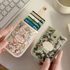 A hand holds a beige leather card wallet with floral print and a wooden pull tab, next to a stack of cards.