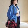 A woman wearing a blue denim shirt and black pants holds a pink and black patterned PU leather tote bag.