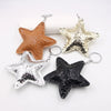 Three star-shaped leather keychains in gold, silver, and black with metal jump rings