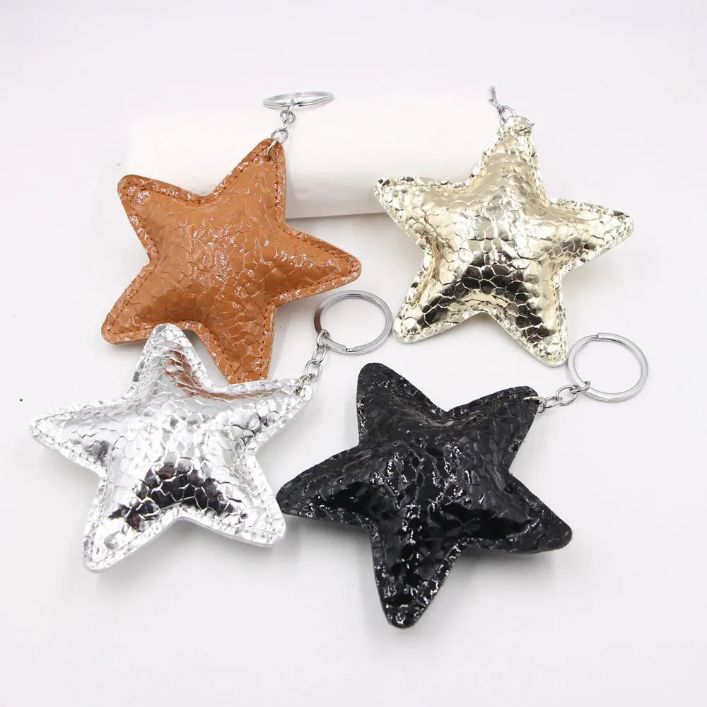 Three star-shaped leather keychains in gold, silver, and black with metal jump rings
