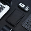 A black magnetic leather card wallet is shown next to a laptop keyboard and a black pen.