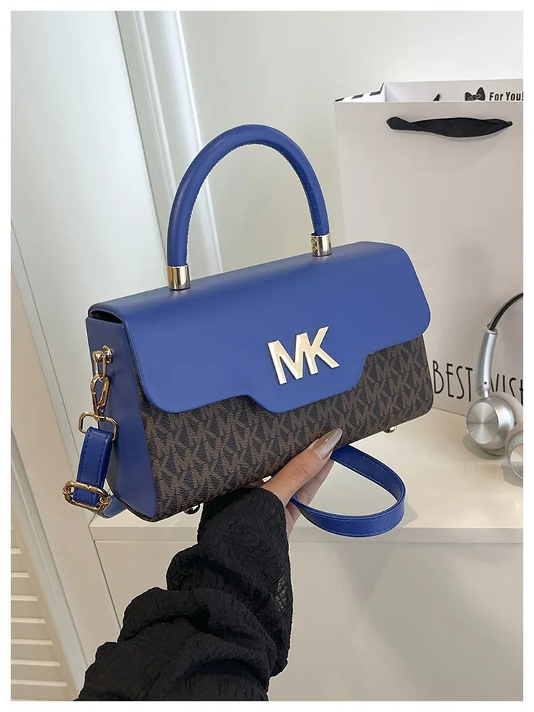 A woman holds a blue Michael Kors letter square crossbody bag with gold hardware against a white background.