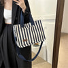 Une femme tient un sac bandoulière à toile rayé marine et blanc contre un manteau noir.