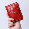 A hand holds a red crocodile pattern leather card holder with a zipper.