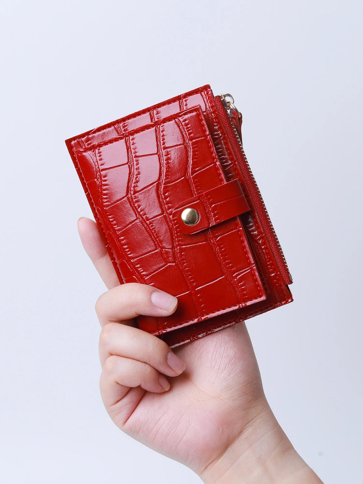 A hand holds a red crocodile pattern leather card holder with a zipper.