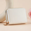 A cream-colored zippered wallet with gold hardware and a quilted texture is shown next to a pale pink flower.