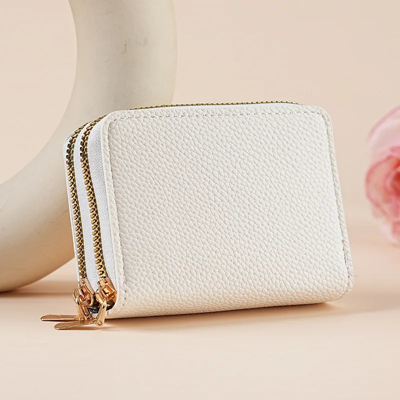 A cream-colored zippered wallet with gold hardware and a quilted texture is shown next to a pale pink flower.