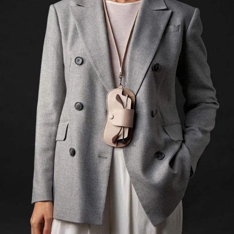 A woman wearing a gray blazer with a light pink top and a leather eyewear storage case necklace.