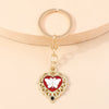 Gold heart-shaped keychain with a white butterfly pendant and a black sun eye detail