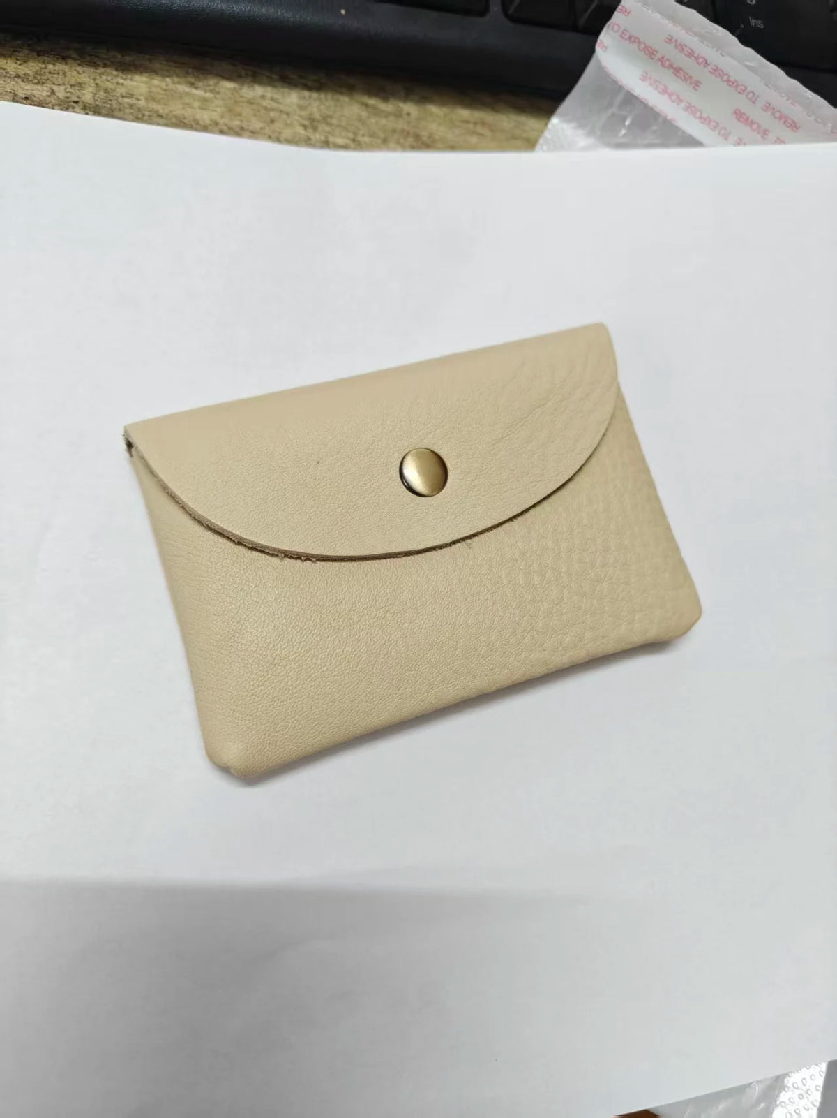 A beige genuine leather card holder with a stitched flap and a round metallic closure.