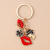 A gold-colored enamel heart keychain featuring a red lip design and a black and gold textured piece.