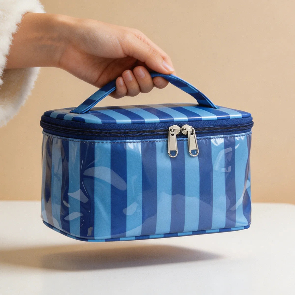 Una mano sostiene una bolsa de almacenamiento de cosméticos y artículos de tocador a rayas azules y blancas.