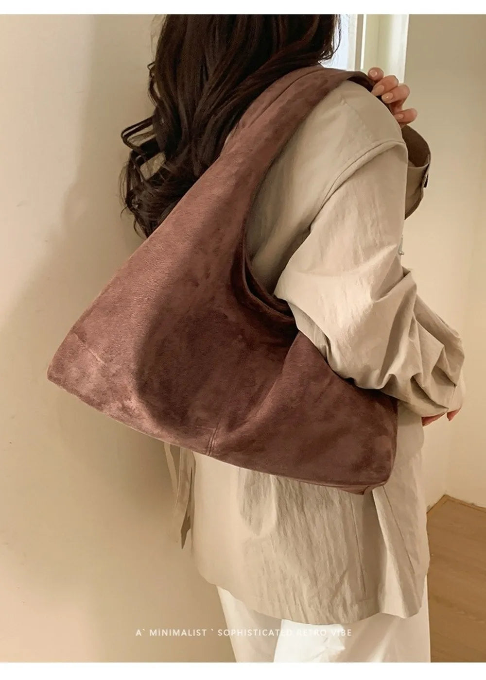 A woman is holding a brown suede shoulder tote bag against a light-colored shirt.