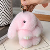 Pink plush rabbit fur keychain with white inner ears being held by a hand