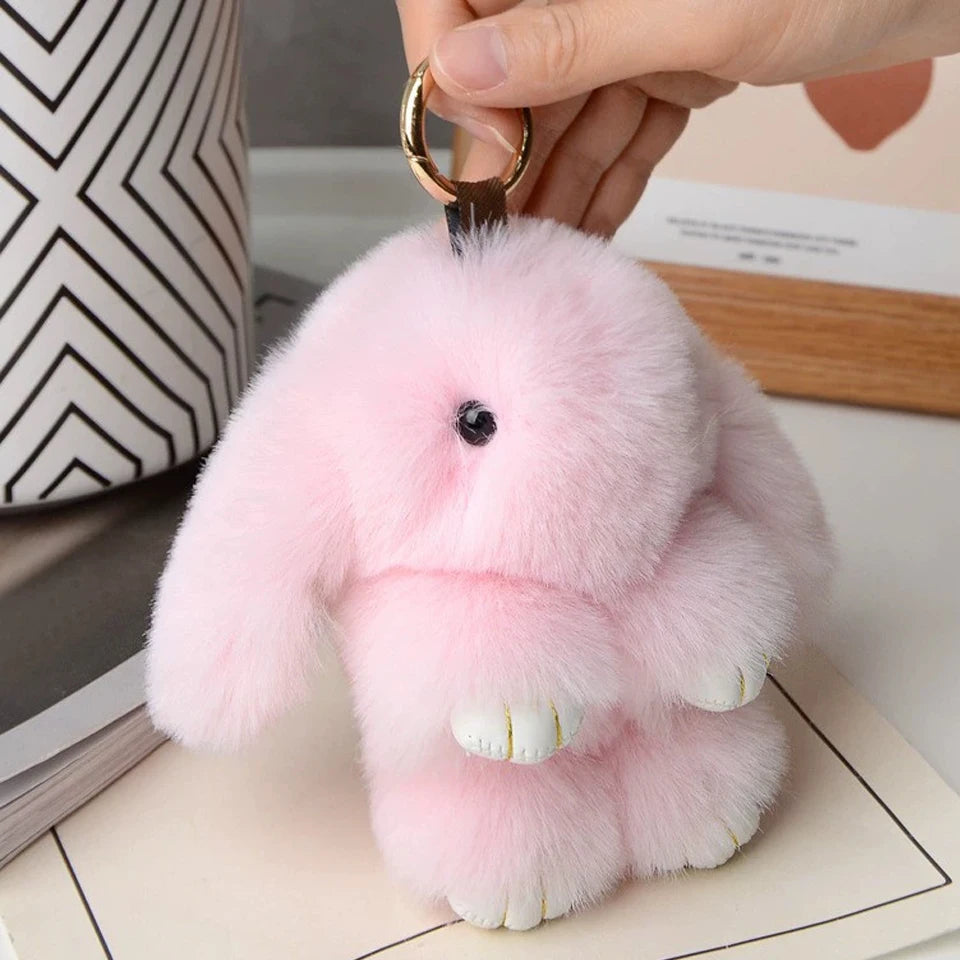 Pink plush rabbit fur keychain with white inner ears being held by a hand