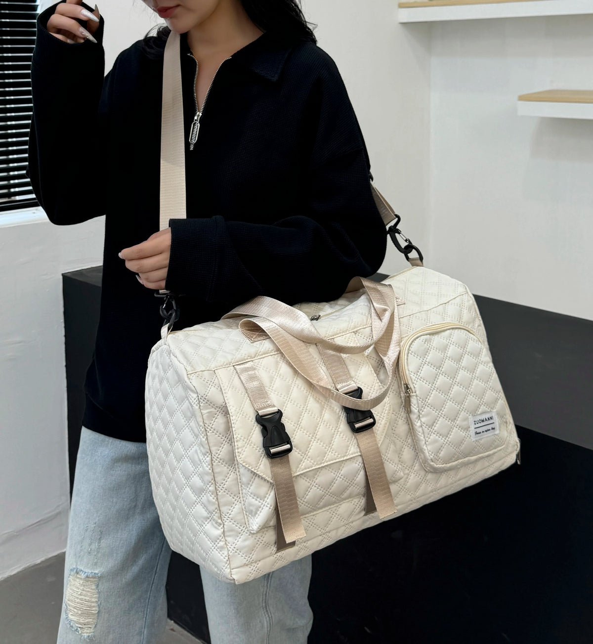 A person holds a cream-colored nylon travel duffle bag with an argyle pattern.