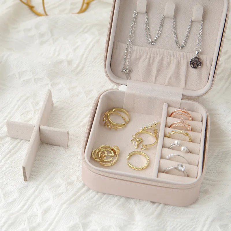 A pink compact leather jewelry travel box with compartments for storing necklaces and rings.